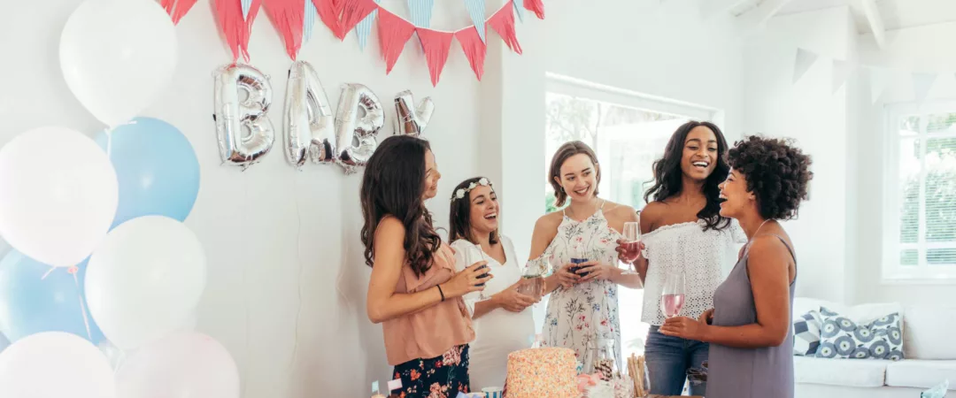 5 femmes dont une femme enceinte en train de rigoler autour d'une table décorée avec un gâteau pour une baby shower