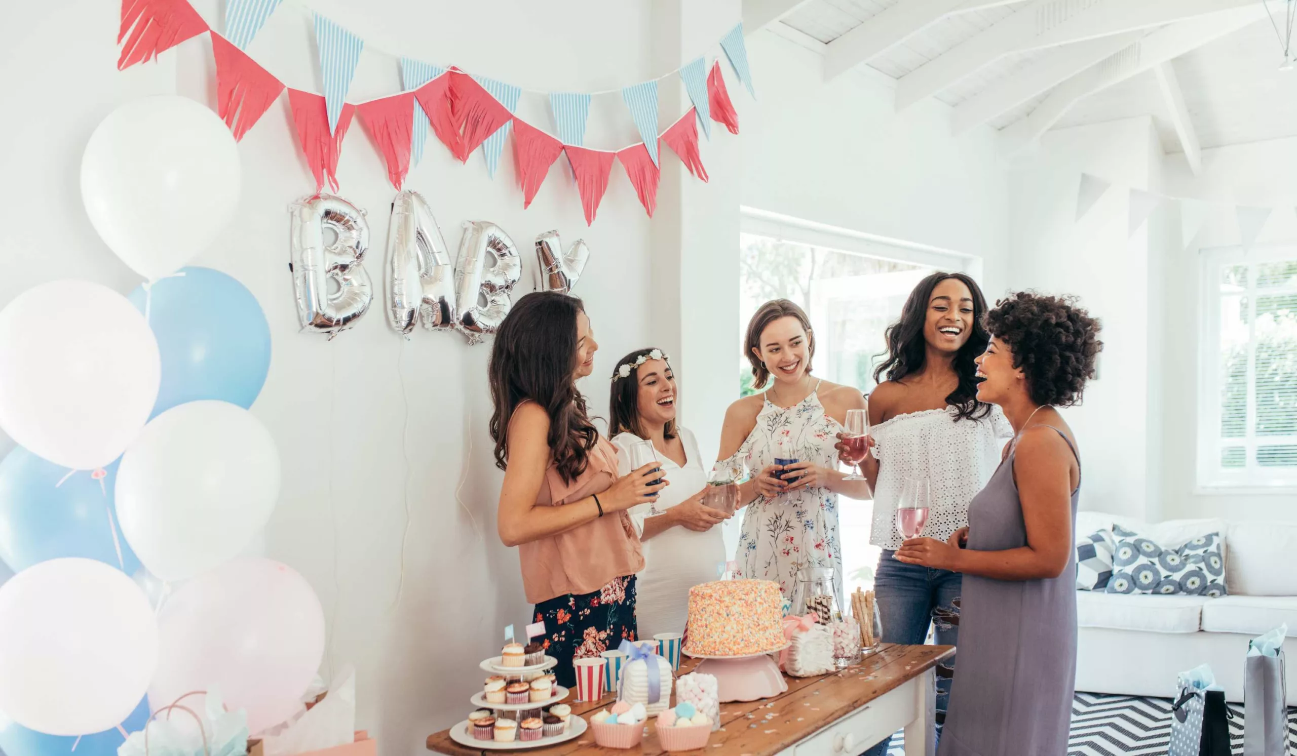 5 femmes dont une femme enceinte en train de rigoler autour d'une table décorée avec un gâteau pour une baby shower